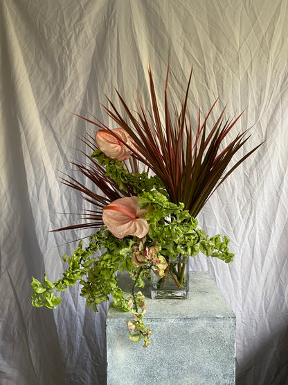 A sculptural botanical arrangement titled Just Another Lovely Day by foRM of Mondays, showcasing an elegant mix of handpicked green leaves and foliage in a clear glass vessel against a minimalist background.