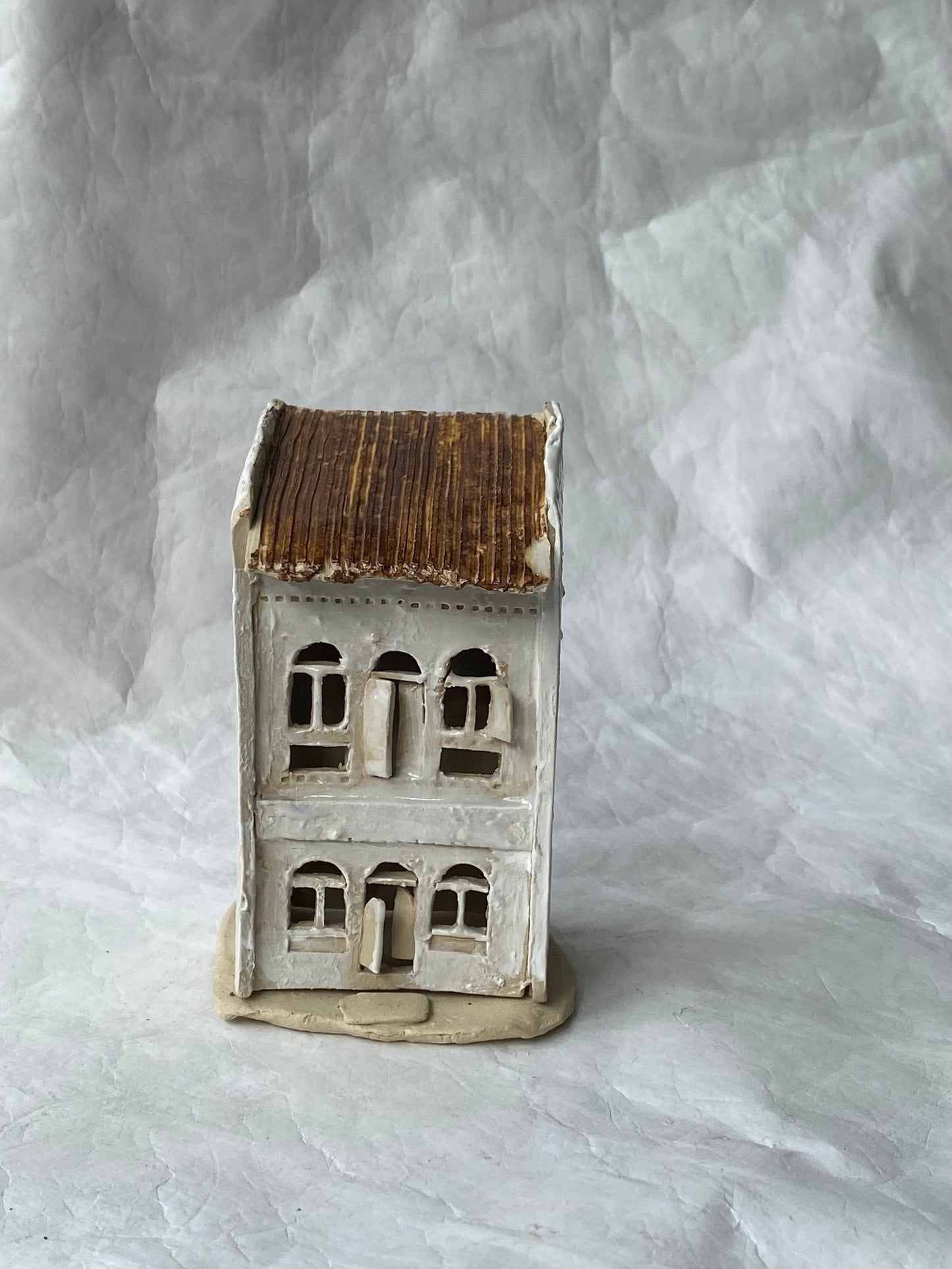 A miniature of Singapore ceramic shophouse figurine with a brown roof and off-white facade, displayed on a textured light gray background.