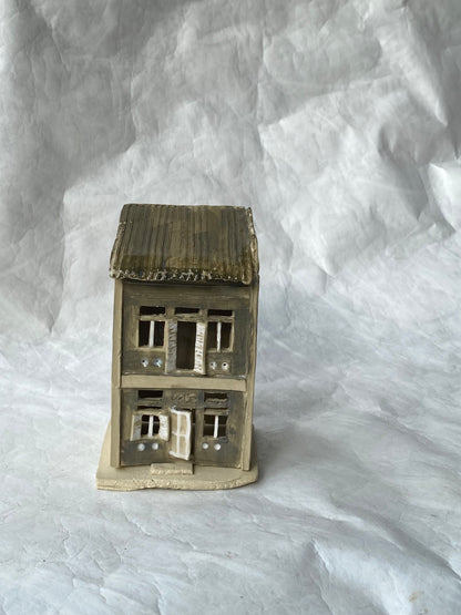 A handbuilt ceramic of Singapore shophouse with a dark ribbed roof and light grey facade, placed on a white paper background.
