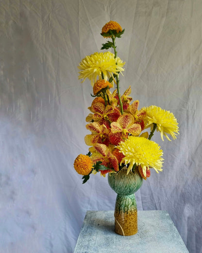 A yellow sculptural floral composition by foRM of Mondays in a ceramic vase on a white background 