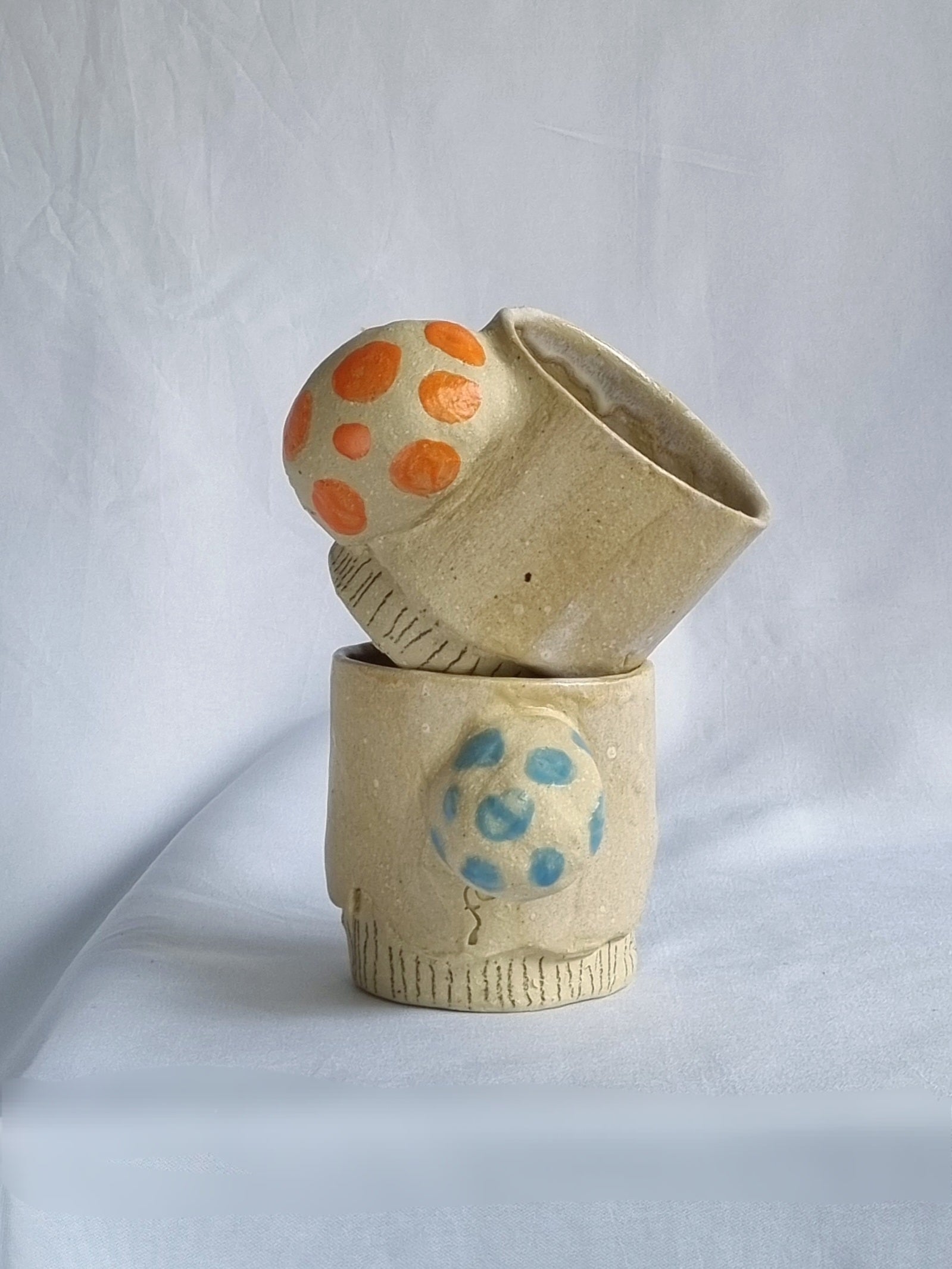 Two ceramic cups with colorful dot patterns on a white background