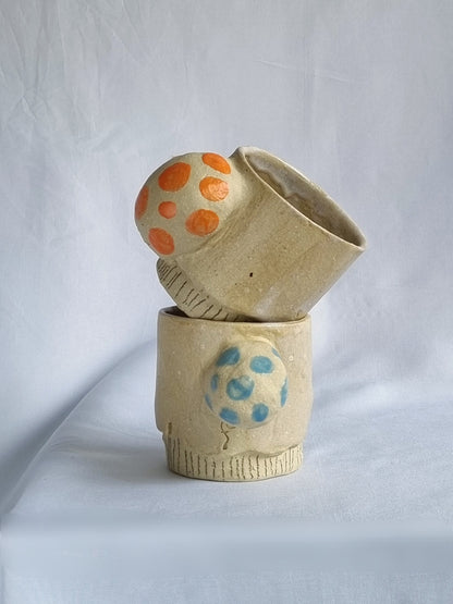Two ceramic cups with colorful dot patterns on a white background