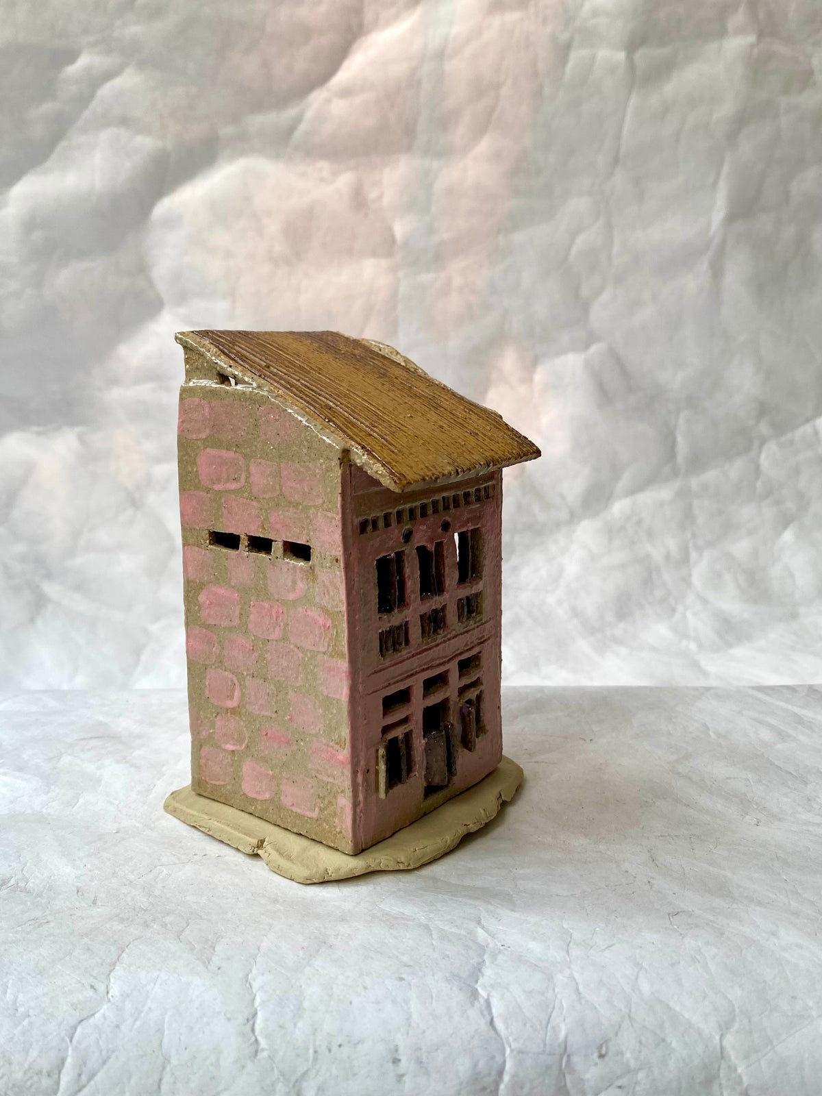 A small handcrafted miniature of Singapore shop house with a pink stone-textured body, brown roof, and beige base, set against a white backdrop.