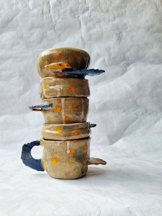 Stack of hand built ceramic cups with decorative patterns, one of a kind, on a textured white background