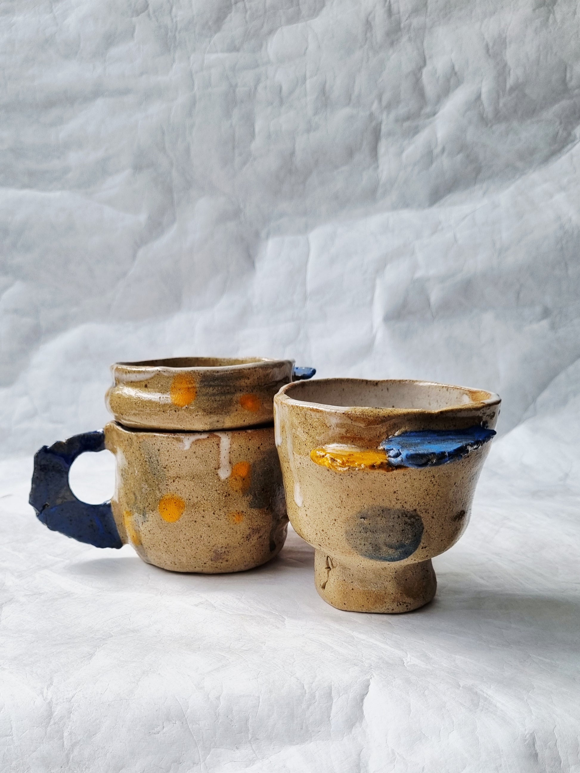 Three unique ceramic cups with abstract designs on a textured white background