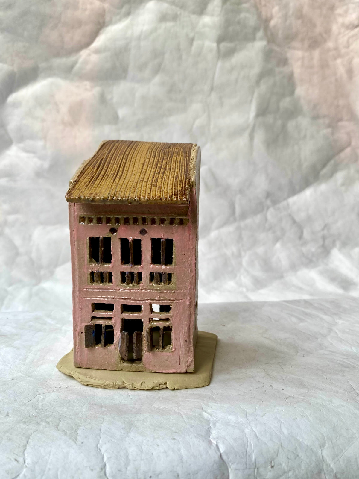 A handbuilt ceramic of Singapore shophouse with a brownribbed roof and pink facade, placed on a white paper background.