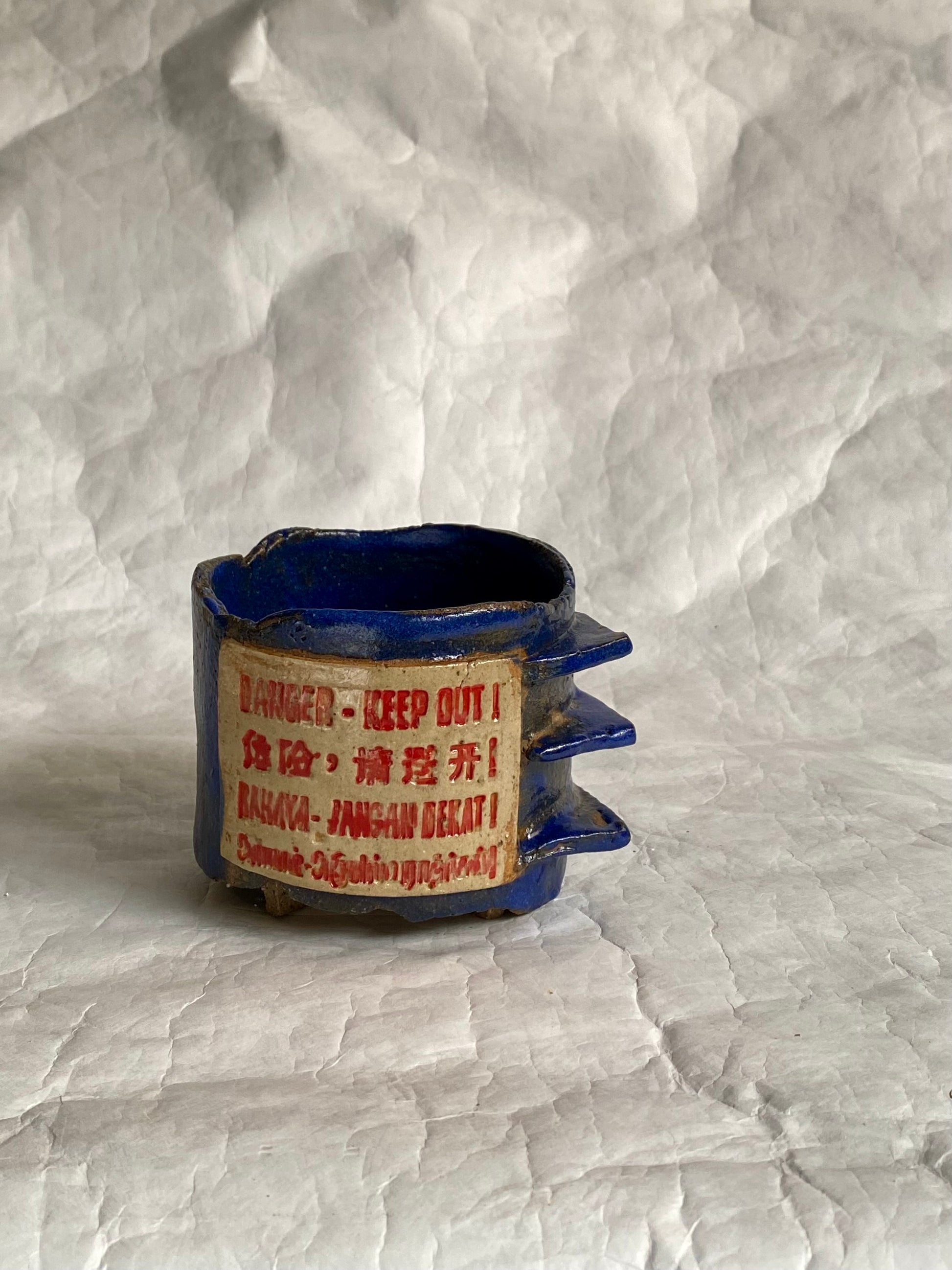 Close-up of hand-carved "Danger- Keep Out”  signage design on a handbuilt ceramic coffee cup.